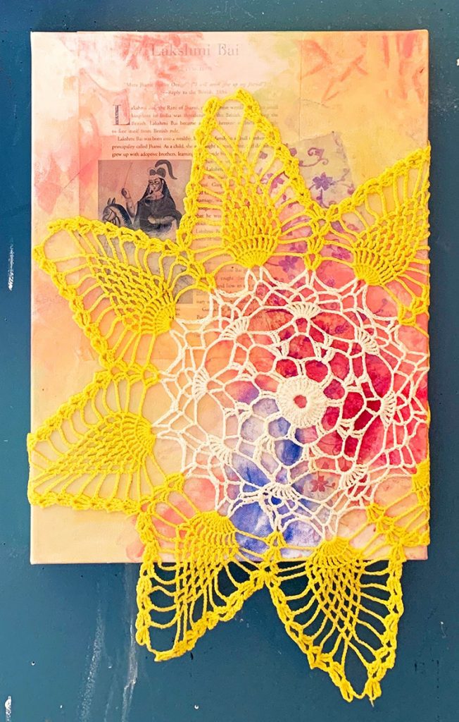 Pink background with Lakshmi Bai in text with an image of a warrior woman on horseback overlaid with a yellow and white star-shaped crochet piece.